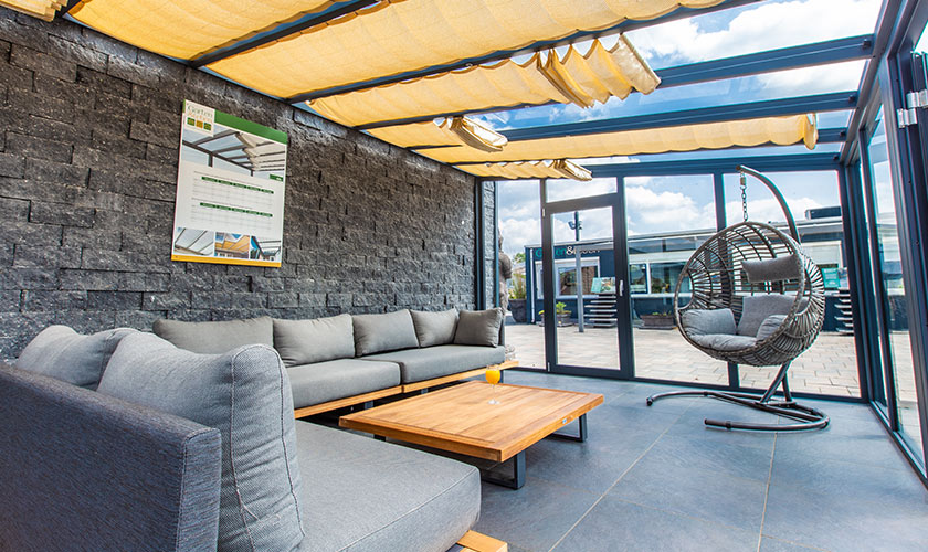Moderner Wintergarten mit grauem Sofa, Holztisch, Hängesessel und Glasdach.