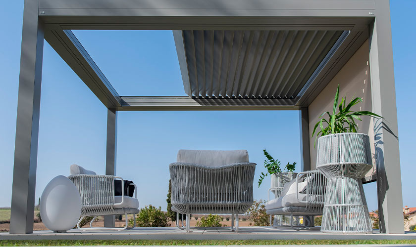 Überdachte Terrasse mit modernen weißen Möbeln und Pflanzen, blauer Himmel im Hintergrund.
