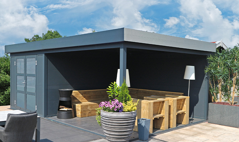 Eine moderne, graue Gartenlaube mit Holzbänken, Pflanzen und blauem Himmel im Hintergrund.
