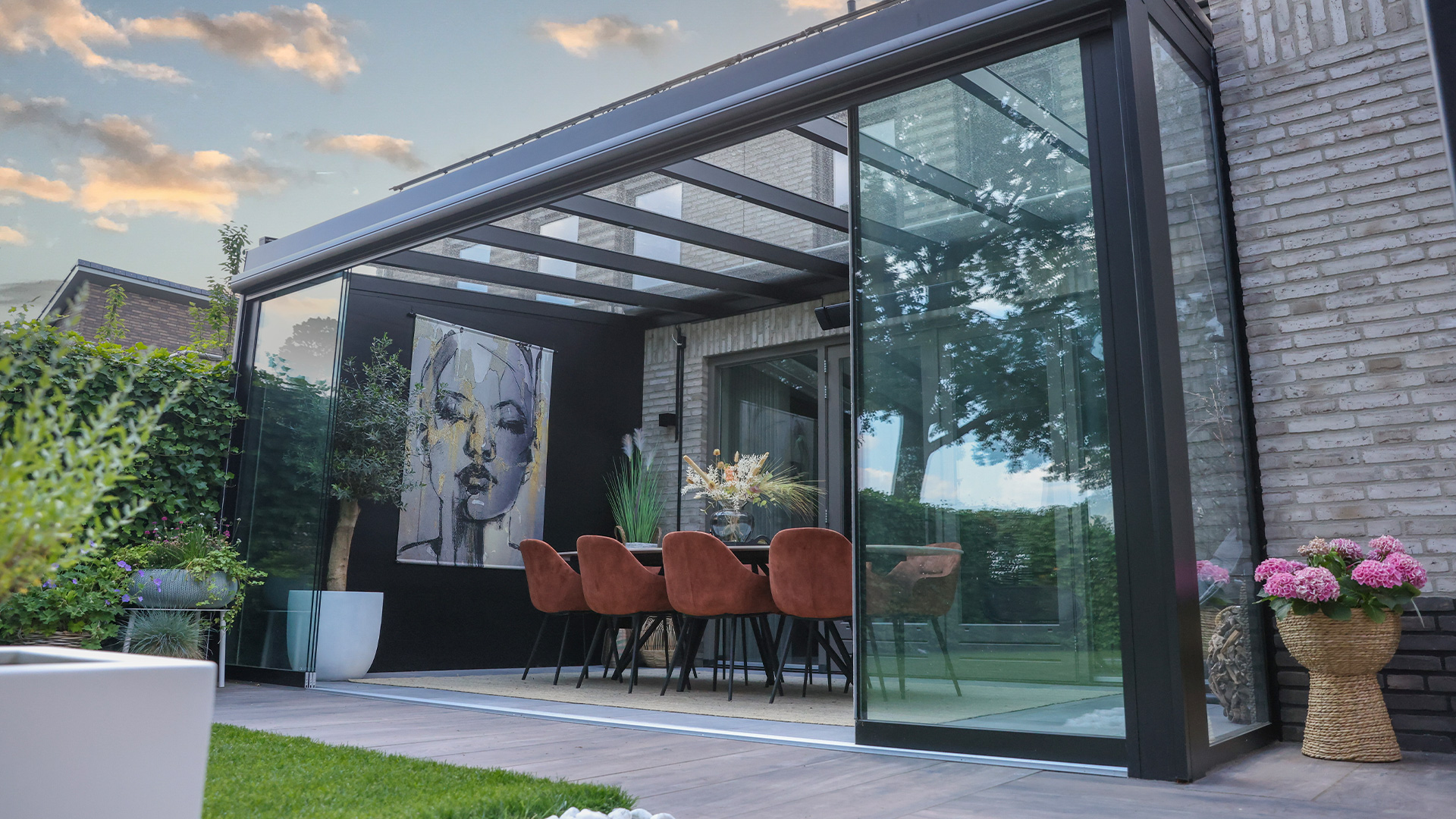 Moderne Terrasse mit Glasanbau, abstraktes Porträtbild, rote Stühle, üppige Pflanzen, Abendstimmung.